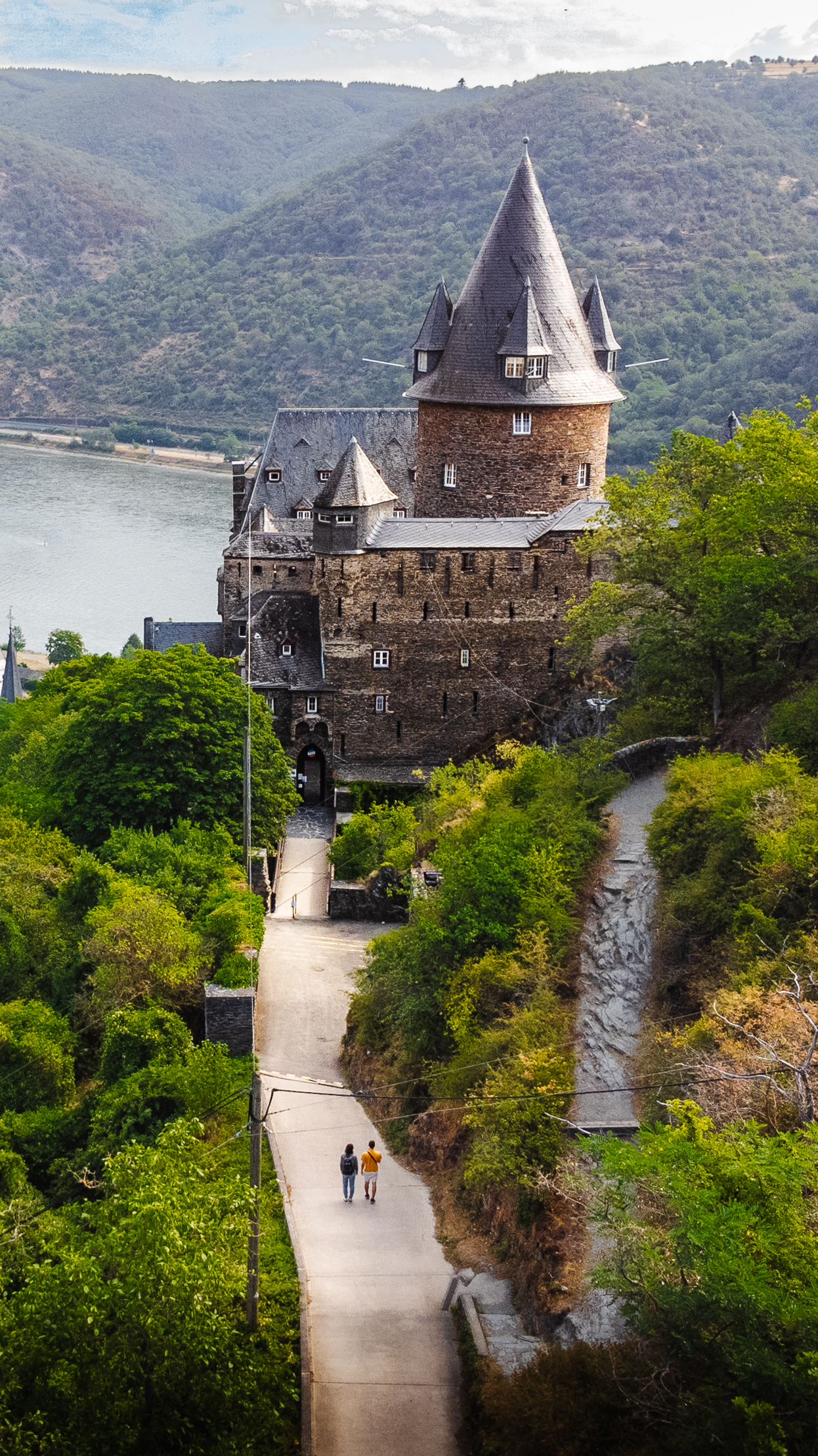 Luftaufnahme von Burg Stahleck mit Pärchen auf dem Zuweg und Rhein im Hintergrund