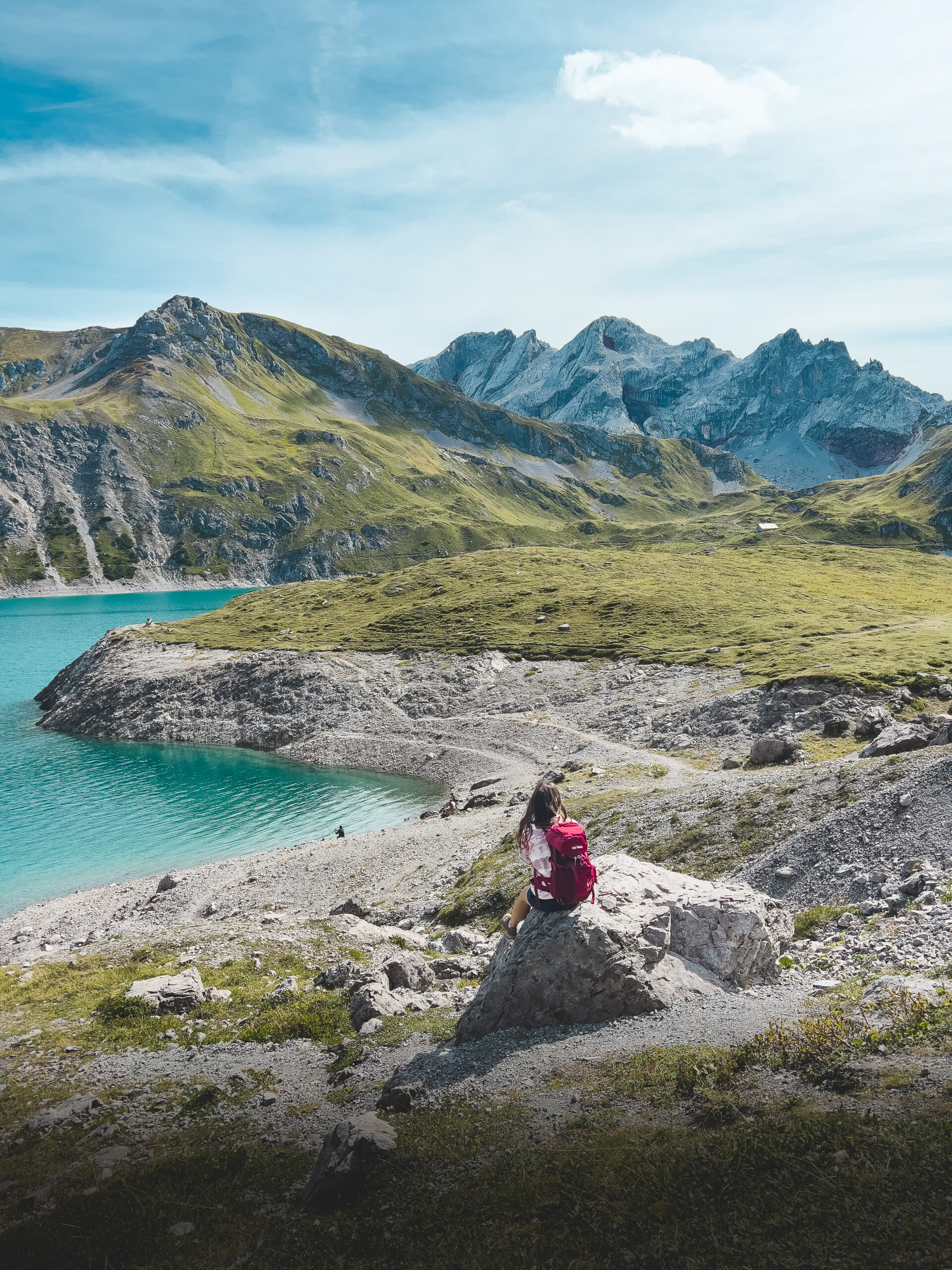 Frau mit rotem Rucksack sitzt vor dem Lünersee in Österreich